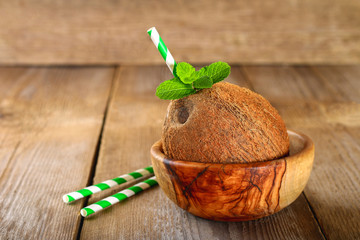 Wall Mural - Coconut with juice inside, mint and green paper tubes on an old wooden table.