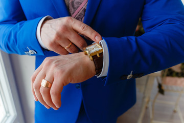 Wall Mural - Man in a blue expensive suit and vest looks at expensive watches. closeup designer watch on businessman hand, he looks on the time and hurrying