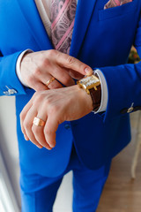 Wall Mural - Man in a blue expensive suit and vest looks at expensive watches. closeup designer watch on businessman hand, he looks on the time and hurrying