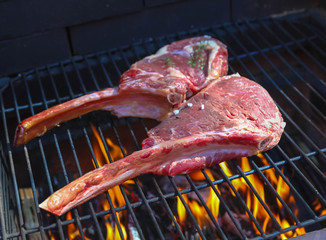 Tomahawk rib beef steak on hot black grill with flames