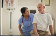© Erickson Stock - Smiling female nurse comforting an elderly male patient inside an exam room.