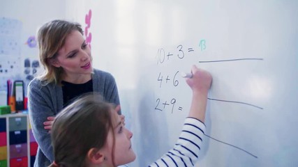 Wall Mural - A small girl with teacher writing on the whiteboard at school.