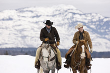 Two Cowboys Riding Horses On Snowy Landscape