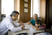 Middle Aged Doctor Talking To A Young Boy And His Mother.
