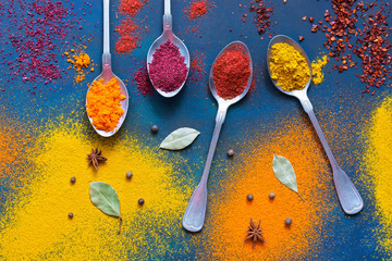 Spices with spoons on a blue background. Bright multicolored background of spices. Top view.