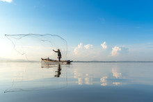 Fisherman Action When Fishing Net On Lake In The Sunshine Morning, Beautiful Blue Sky Background. Thailand