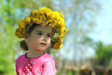 Wall Mural - Springtime portrait of a cute two years old girl posing with a dandelion wreath