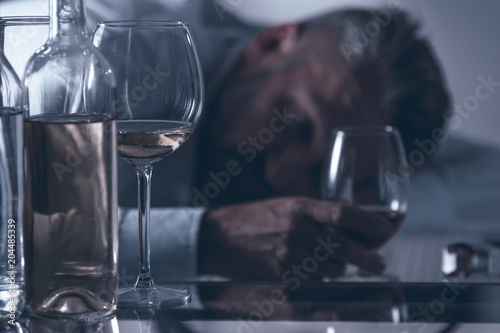 Fotografia, Obraz Close-up of a drunken desperate middle-aged man leaning on the table behind bott