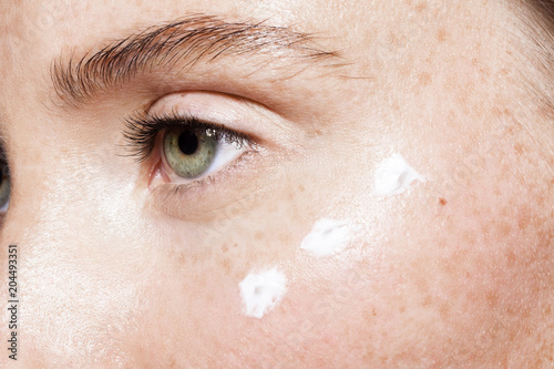 Fotografia Close up of beautiful woman face with clean fresh skin and points of white moisturizing cream under eye