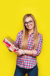 Smiling young stylish student is standing with books on yellow background in glasses and casual bright outfit