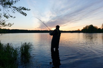 Silhouette of fisherman standing in the lake and catching the fish during sunrise