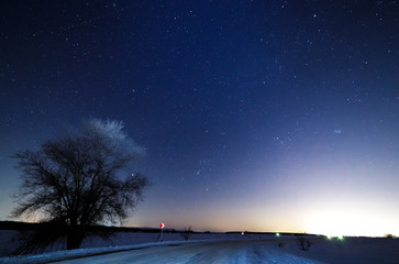 Stars in the sky above the snowy road. Street lights in the background.