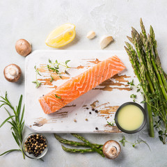 Wall Mural - Overhead shoot with fresh green asparagus, raw salmon fillet, herbs and sauce and old white wooden board. Healthy food background, copy space, top view.