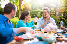 Group Of Friends Gathered Around A Table In A Garden On A Summer Evening To Share A Meal And Have A Good Time Together