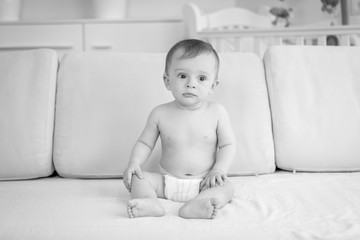 Wall Mural - Black and white photo of sad baby boy indiapers sitting on sofa