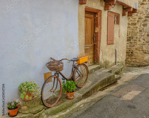 Fototapeta na szkło Sant Antonin de Noble Val, Midi Pireneje, Francja - 23 lipca 2017 r .: Dekoracyjny rower z kwiatami spoczywa na rustykalnej fasadzie wioski