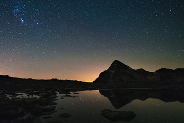 Wall Mural - astro starry sky reflected on lake at high altitude on the alps. orion constellation glowing.