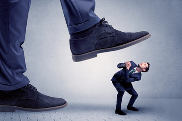  Young handsome businessman getting crushed by a big formal shoe
