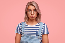 Cute Adorable Woman With Unhappy Expression, Curves Lips As Being Victim Of Sexual Abusement, Wears Casual Clothes, Isolated Over Pink Studio Background. Discontent Caucasian Girl With Dyed Hair