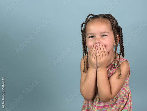 Fotografie, Obraz Adorable girl with hands over mouth on blue background with room for copy