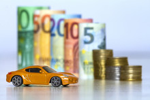 Blurred Row Of Rolled Hundred, Fifty, Twenty, Ten And Five New Euro Banknotes And Pile Of Coins With Yellow Toy Expensive Sport Car. Symbol Of Financial Prosperity, Vehicle Sale And Purchase.