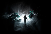 Man With Riffle At Spooky Forest At Night. Strange Silhouette Of Hunter In A Dark Spooky Forest At Night, Mystical Landscape Surreal Lights With Creepy Man . Selective Focus