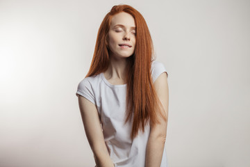 Wall Mural - Portrait of a cheerful young redhaired emotional woman dreaming with closed eyes in positive mood over white background