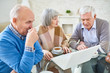 © Seventyfour - Elegant senior woman and men drinking tea and surfing laptop together sitting at table in assisted living home.