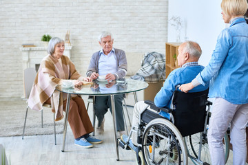 Nurse entering room with senior man in wheelchair introducing him to patients of assisted living home. 