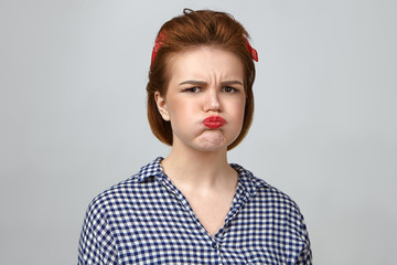 Wall Mural - Horizontal studio portrait of irritated pretty girl in her twenties expressing dissatisfaction, blowing cheeks and pouting lips, feeling offended by husband who didn't take her to party with him