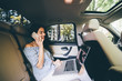 © F8  \ Suport Ukraine - Businesswoman sitting on back seat of car with laptop talking on mobile phone. Female executive travelling to work in luxury car.