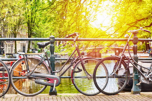 Plakat Bicykle na moscie w Amsterdam, holandie przeciw kanałowi z światłem słonecznym. Pocztówka z Amsterdamu. Pojęcie turystyki.