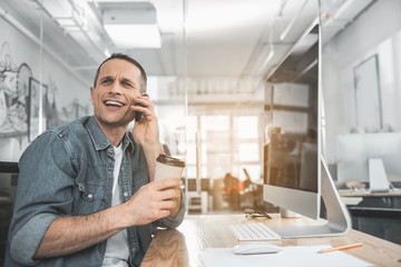Poster - Portrait of smiling man speaking by mobile while drinking cup of coffee in office. Employer working with appliance concept
