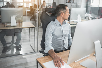 Poster - Side view pensive male using digital device while sitting at table in office. Wistful worker at job concept