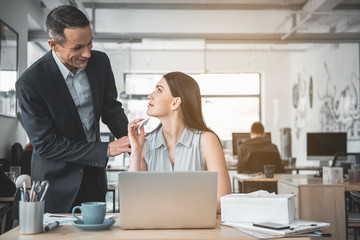 Aufkleber - Outgoing boss telling with smiling secretary. She sitting at table and working with notebook computer. Professional communication concept