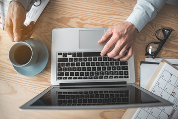 Poster - Top view close up employer arms using laptop and keeping mug of liquid