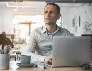 Poster - Portrait of thoughtful employer typing in laptop while sitting at desk in office. Wistful employer during labor concept