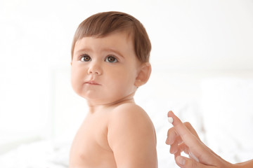 Wall Mural - Woman applying body cream on her baby against light background