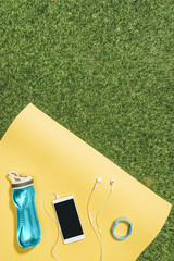 Wall Mural - flat lay with water bottle, watch, smartphone and earphones on yellow mat on green lawn