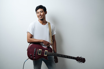 Pretty guy with guitar wearing white blank t-shirt, empty wall, horizontal studio portrait