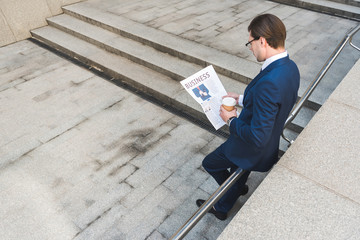 high angle view of young businessman with coffee to go reading newspaper