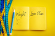 Weight loss and Diet control concept background. Colorful of Measuring tape on vibrant yellow color  background with blue book diary notepad and text as 