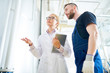 © Seventyfour - Pretty fair-haired factory worker wearing white coat discussing equipment occurrences with bearded technician while standing at spacious production department, low angle view