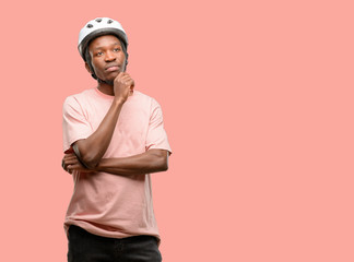 Poster - Black man wearing bike helmet thinking and looking up expressing doubt and wonder