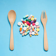 Top view of pharmaceutical medicine pills, capsules and tablets w/ wooden spoon and fork on light blue background. Vitamin and supplement for health care. Health behavior concept. Minimal style.