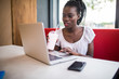 © F8  \ Suport Ukraine - Portrait of afro american student female typing answers to friends while working on a laptop with wireless internet connection drinking milkshake in cafe