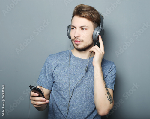 Fotografie, Obraz Man holding mobile phone and lictening to music over grey background