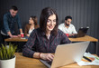 © proimagecontent - Portrait of brunette girl wears eyeglasses using silver laptop computer before office colleagues, indoor shot of working atmosphere