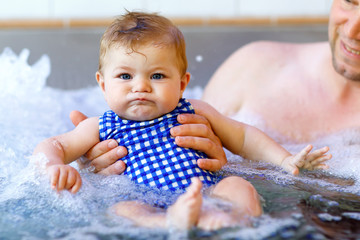 Wall Mural - Happy middle-aged father swimming with cute adorable baby girl in swimming pool.