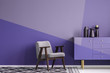 Real photo of a gray, wooden armchair on patterned, black and white rug in creative living room interior with geometric, violet wall and cupboard
